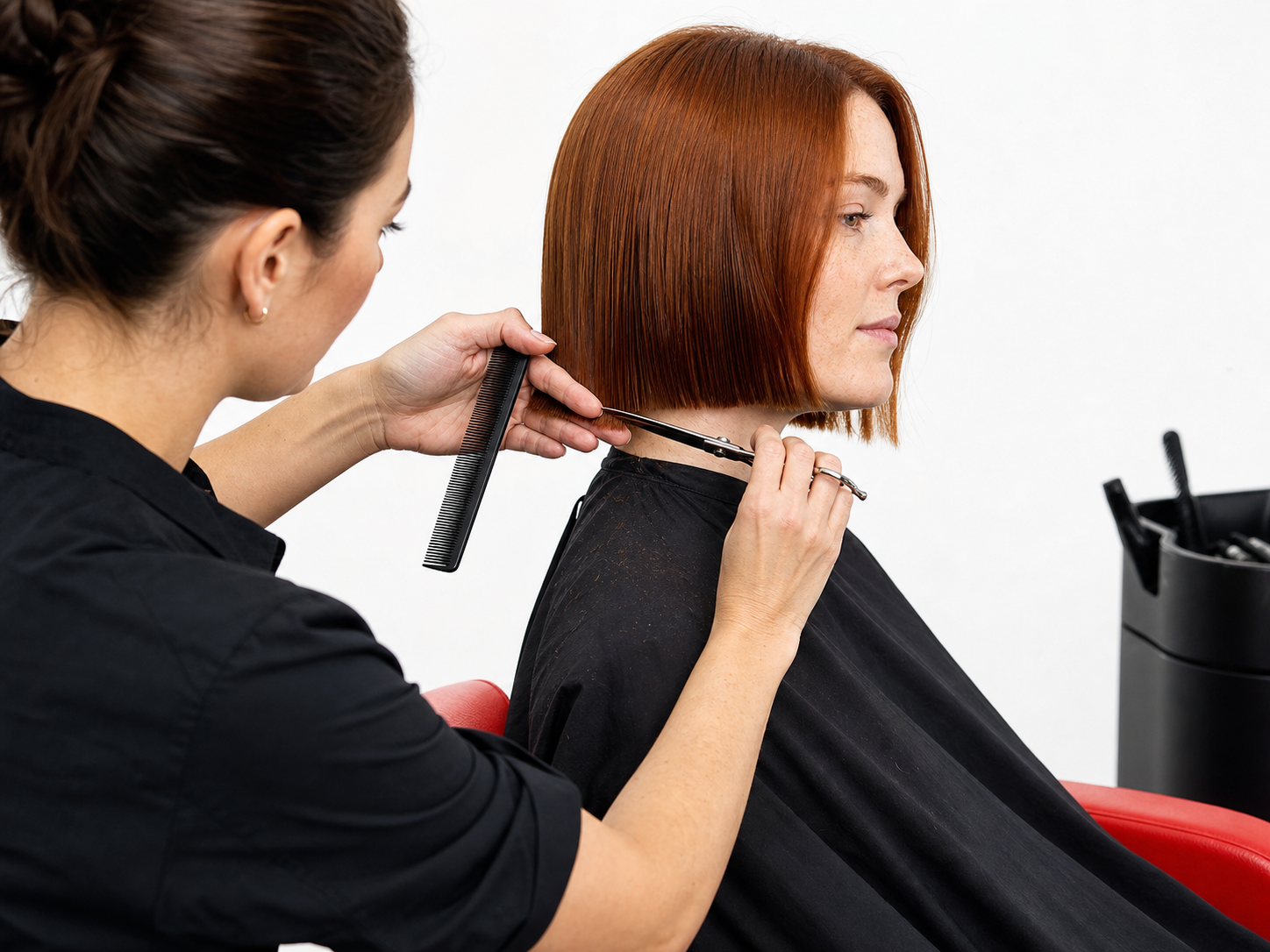 A woman stylist refining a red chin-length bob with scissors and comb